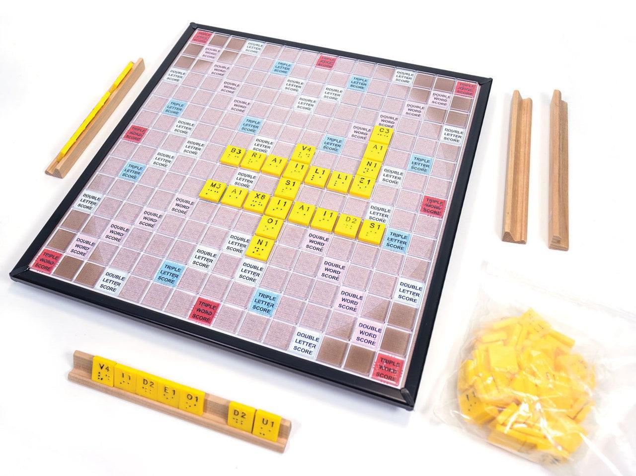 Braille version Scrabble board with yellow tiles that combine the printed letter, its numeric value and raised braille dots; on the sides, wooden tile racks with letters and a spare tile bag.