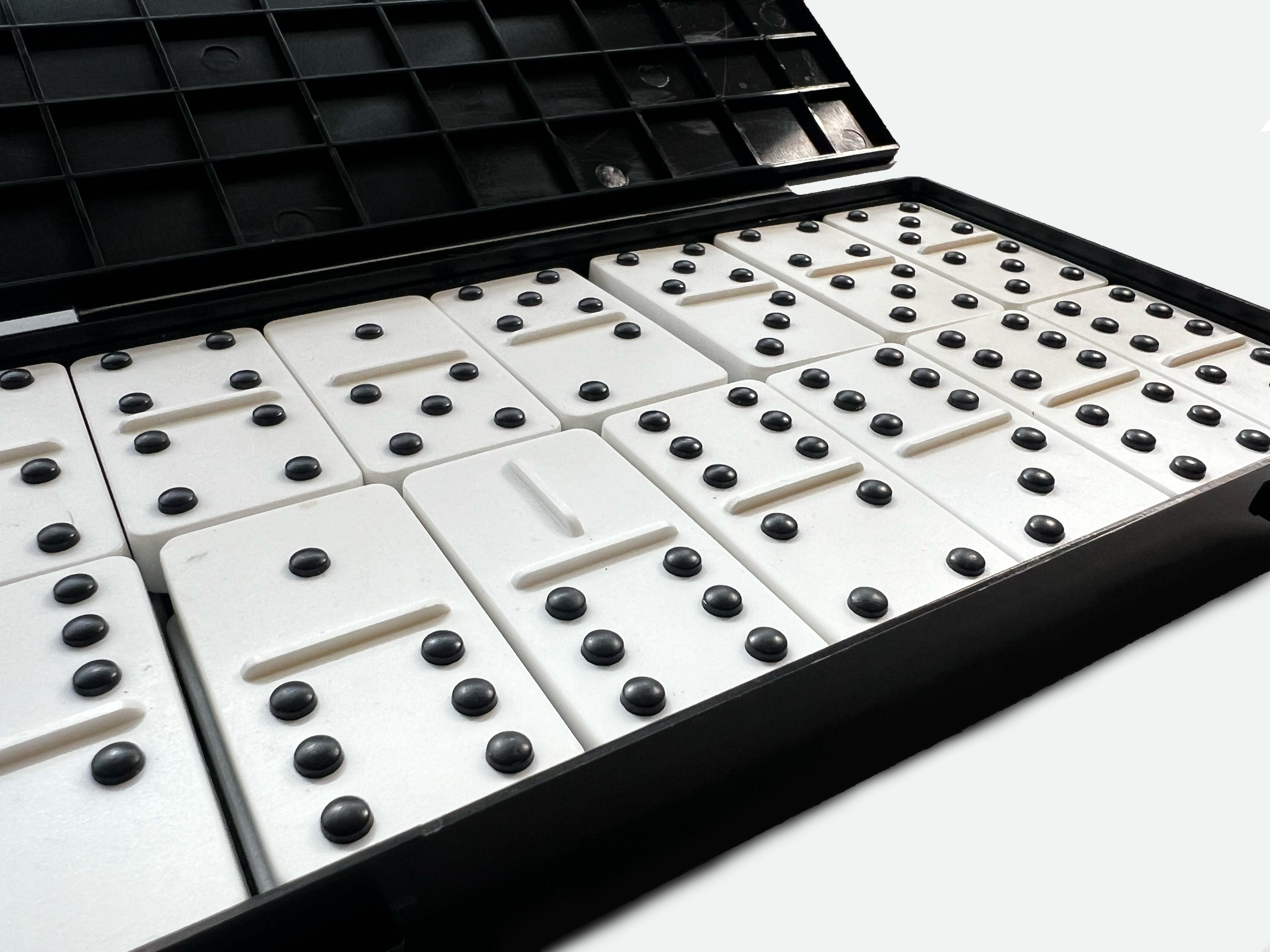 Close-up of a domino set with raised black dots on white tiles, arranged in rows inside their open black storage case.